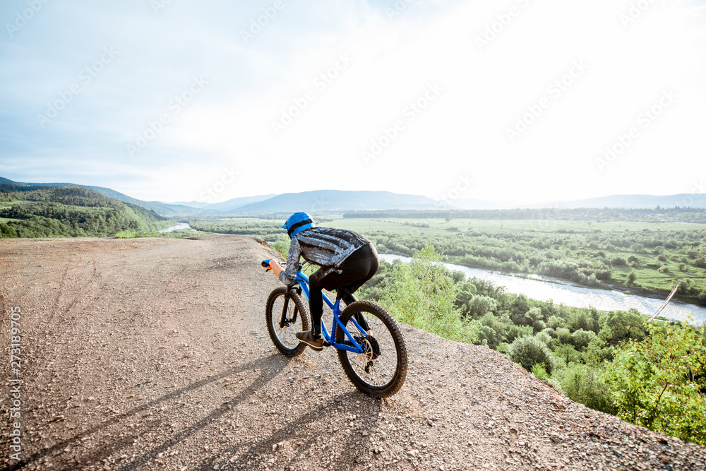 Professional well-equipped cyclist riding bicycle on the rocky mountains with beautiful landscape view during the sunset Professional well-equipped cyclist riding bicycle on the rocky mountains with beautiful landscape view during the sunset