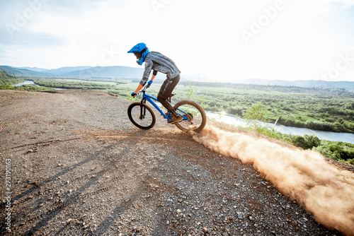 Professional well-equipped cyclist riding extremely on the rocky mountains raising dust behind during the sunset