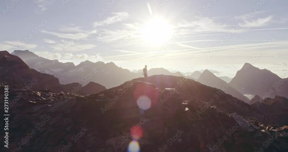 Aerial trail runner man standing on mountain top peak goal looking horizon view.drone shot.Wild nature outdoors at sunrise or sunset backlit.Training activity,sport,effort,challenge,willpower concepts