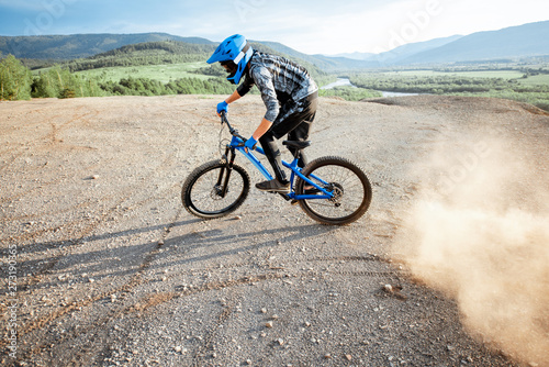 Professional well-equipped cyclist riding extremely on the rocky mountains raising dust behind during the sunset