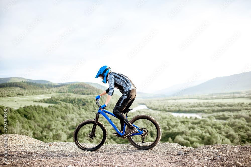 Professional well-equipped cyclist riding bicycle on the rocky mountains with beautiful landscape view during the sunset