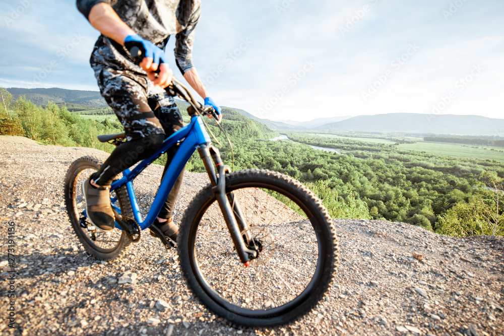 Professional well-equipped cyclist riding bicycle on the rocky mountains with beautiful landscape view during the sunset. Cropped image with no face