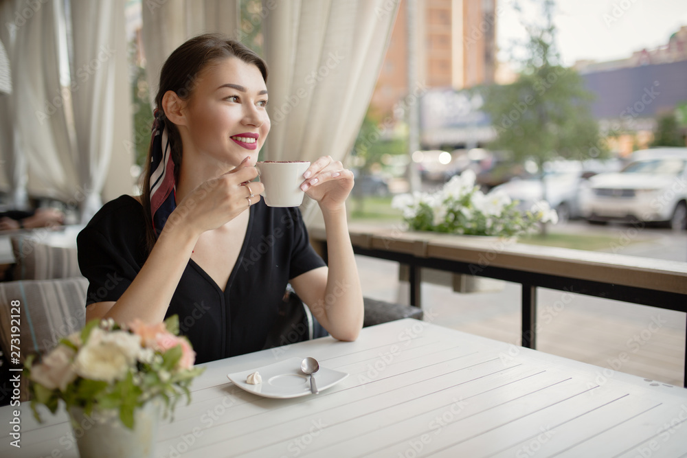 Young beautiful woman with a smile sits on the street and drinks coffee. Summer bright cafe. Young beautiful woman with a smile sits on the street and drinks coffee. Summer bright cafe.