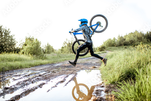 Professional well-equipped cyclist jumping through the puddle on the mountain dirt road during the sunset