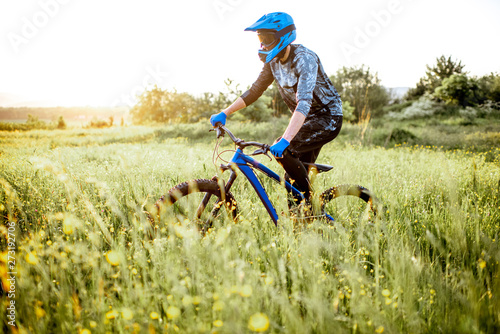 Professional well-equipped cyclist riding on the beautiful green field on the mountains during the sunset