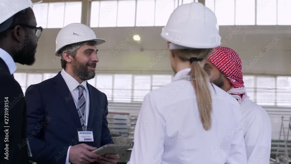 All-round shot of multi-ethnic engineers staying at building in helmets and discussing plans of collaboration All-round shot of multi-ethnic engineers staying at building in helmets and discussing plans of collaboration