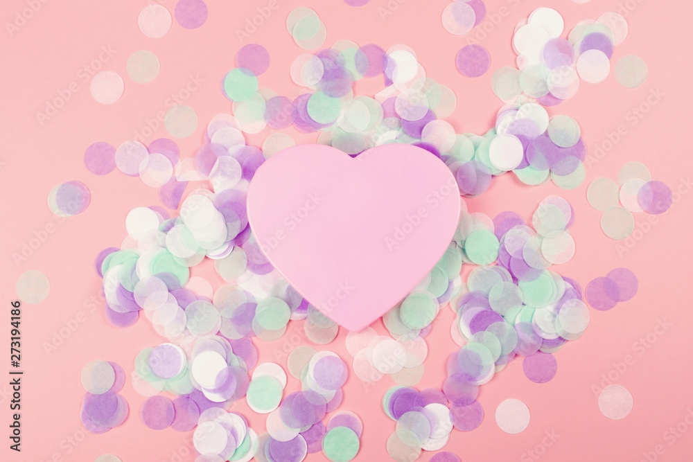 Plastic heart on pink background with confetti.