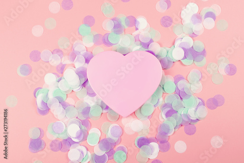 Plastic heart on pink background with confetti.