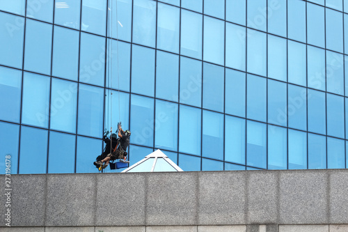 Male worker in overalls professional repair the windows in high-rise. Worker washing windows in office building. Washer wash the windows of modern skyscraper, high risk work