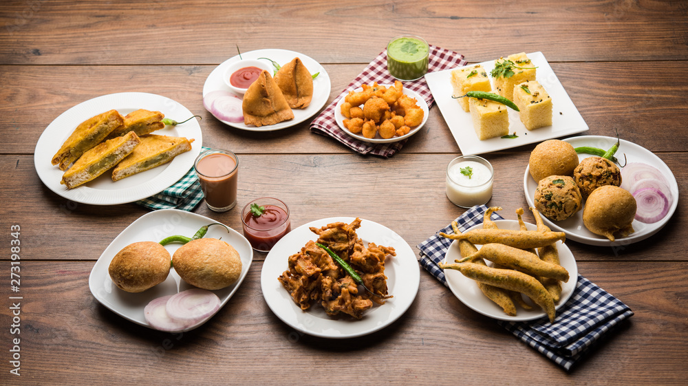 Indian Tea time snacks  in group includes Veg Samosa, Kachori/kachaudi, aloo bonda, khaman dhokla, bread, onion,chilli and moong pakora/pakoda/bhaji/bhajji/Bhajiya/bajji with sauces, selective focus