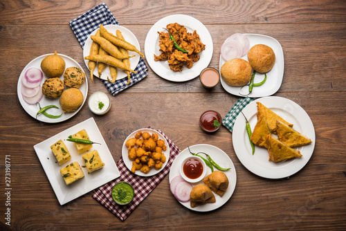 Indian Tea time snacks  in group includes Veg Samosa, Kachori/kachaudi, aloo bonda, khaman dhokla, bread, onion,chilli and moong pakora/pakoda/bhaji/bhajji/Bhajiya/bajji with sauces, selective focus photo