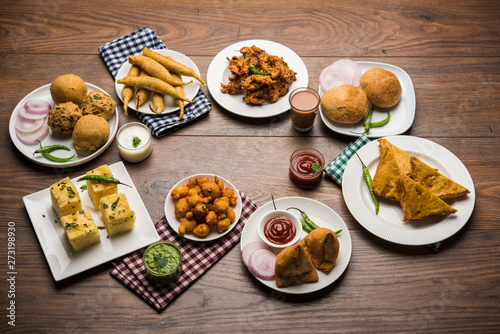 Indian Tea time snacks in group includes Veg Samosa, Kachori/kachaudi, aloo bonda, khaman dhokla, bread, onion,chilli and moong pakora/pakoda/bhaji/bhajji/Bhajiya/bajji with sauces, selective focus