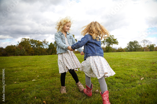 two sisters holding hands spinning together in a field photo