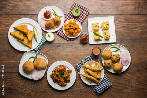 Indian Tea time snacks in group includes Veg Samosa, Kachori/kachaudi, aloo bonda, khaman dhokla, bread, onion,chilli and moong pakora/pakoda/bhaji/bhajji/Bhajiya/bajji with sauces, selective focus