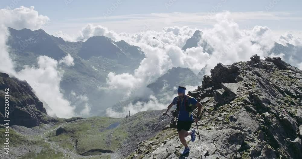 Aerial of man run on ridge edge.Trail runner running to mountain top peak training on rocky cliff.Wild green nature outdoors at sunrise or sunset backlit. Activity,sport,effort,challenge,willpower
