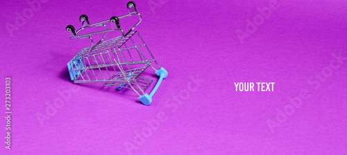 Minimalist shopping concept. Empty inverted miniature shopping trolley on purple background. Copy space photo