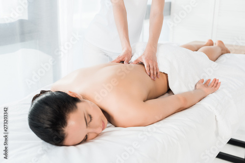 cropped view of masseur doing massage to attractive brunette girl lying on massage table
