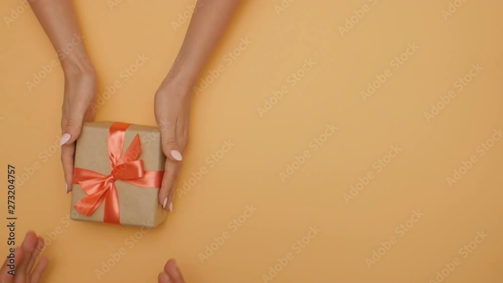 girl gives a box to a man, congratulating the hands of a young couple, top view on a color studio background, concept of holidays and love