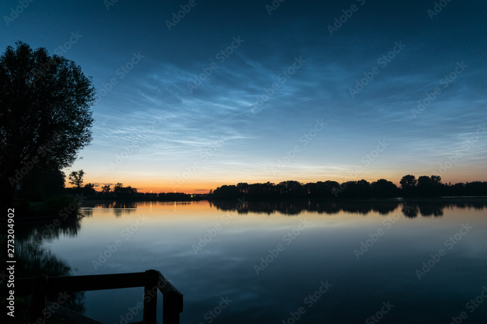 Obraz premium Scenic view of noctilucent clouds (NLC, shining night clouds) over a lake in Holland around midnight.