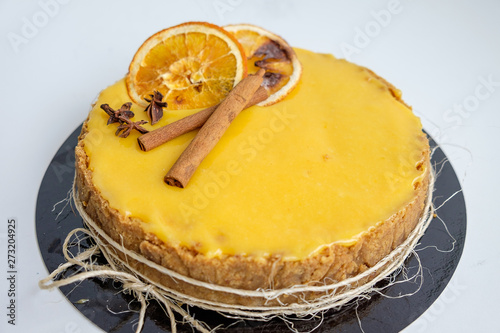 top view at an angle of the cake rich yellow-orange decorated with cinnamon sticks and a piece of orange isolated