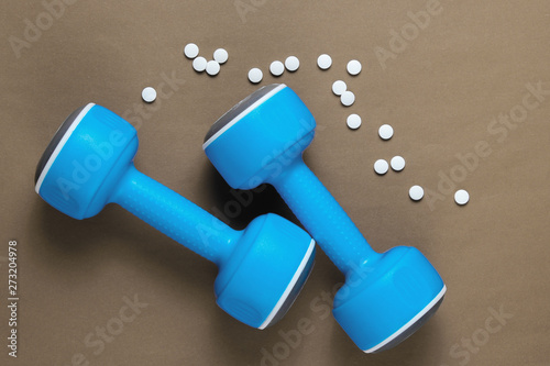 Sport concept. Dumbbells, pills on brown background. Minimalism. Top view