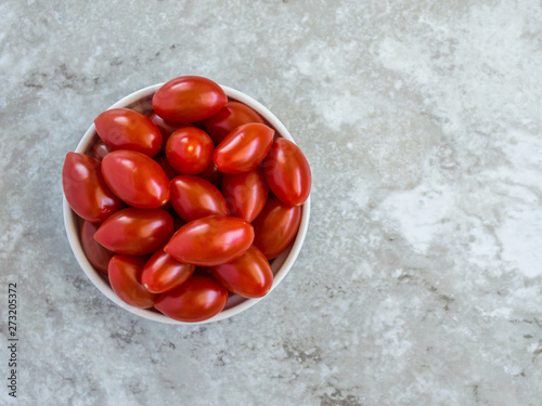 small bowl filled with bright red grape tomatoes on a gray marble counter viewed from above with copy space