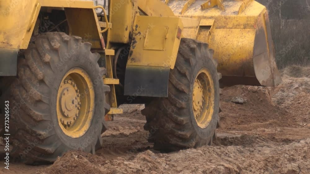 Yellow big construction loader levels a piece of land for construction and collects land in a bucket, industry, construction equipment