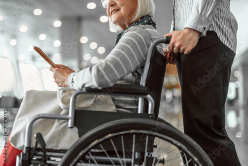 Female worker of airport holding wheelchair with elderly lady