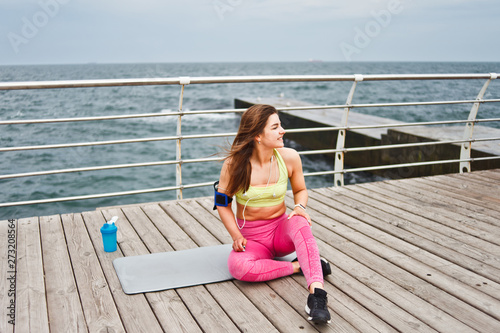 Young fit woman in sportwear sitting on a mat and resting on the beach