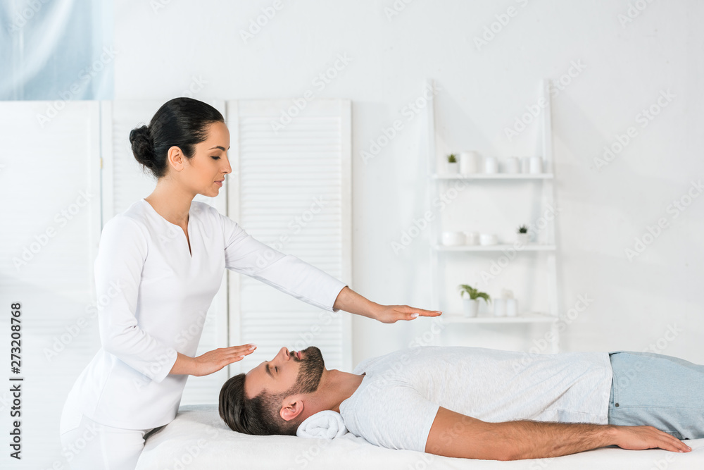 attractive healer putting hands above body of handsome man on massage table attractive healer putting hands above body of handsome man on massage table