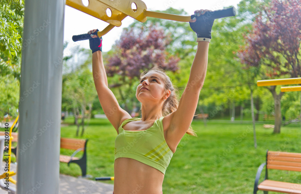 Obraz premium Young woman pulls herself up on a horizontal bar in the park