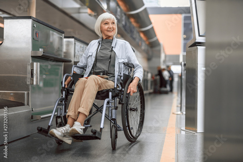 Cheerful mature woman on disabled carriage moving near check-in counter