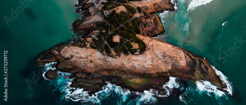 Rock formation on the coast of Rio de Janeiro locally known as Arpoador, harpooner, in the neighbourhood of Ipanema seen from above while ocean waves are crashing into it photo