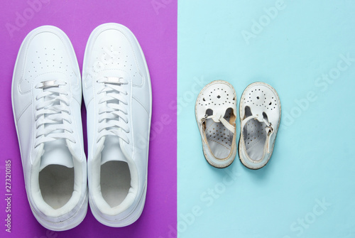 Father's day concept. Adult white sneakers and children's sandals on purple blue background. Top view