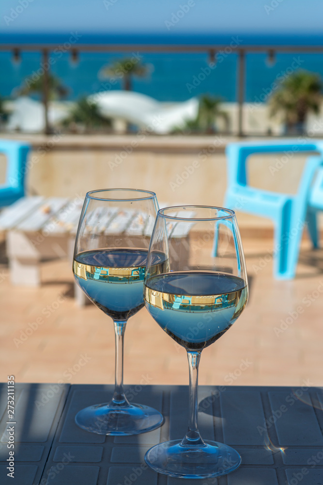 Two wine glasses with white wine served on outdoor terrace witn blue sea and mountains view on background Two wine glasses with white wine served on outdoor terrace witn blue sea and mountains view on background