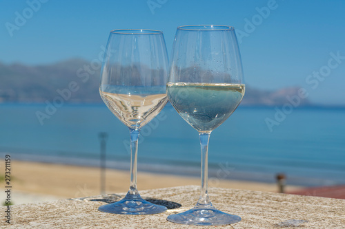 Two wine glasses with white wine served on outdoor terrace witn blue sea and mountains view on background