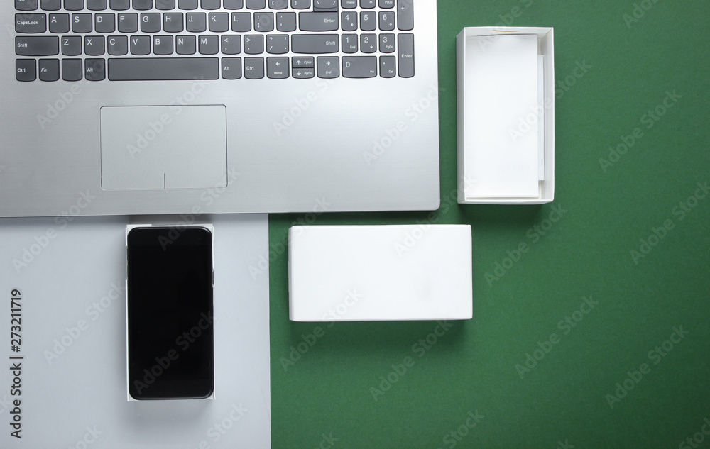 The concept of unboxing, techno blogging. Box with new smartphone, laptop on green background. Top view