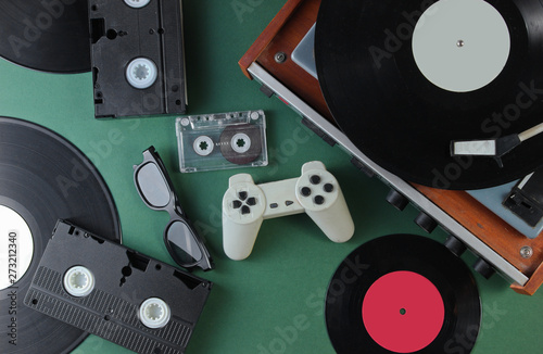 Retro media and entertainment items 80s. Vinyl player, Video, audio cassettes, 3D glasses, gamepad on green background. Top view