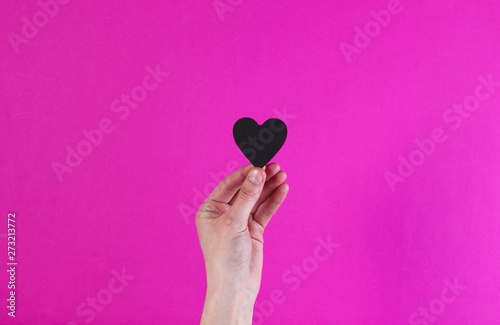 Female hands hold black decorative heart on pink background