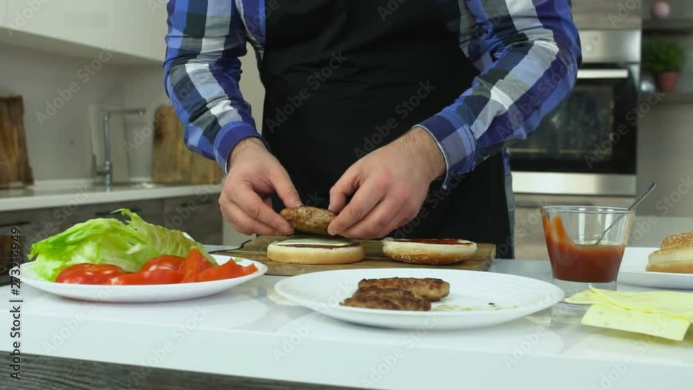 Overweight man cooks hamburgers at home. Plump guy puts a cutlet on a bun. Unhealthy Lifestyle, fried and high calorie harmful food. The risk of obesity and overweight. Slow motion. Overweight man cooks hamburgers at home. Plump guy puts a cutlet on a bun. Unhealthy Lifestyle, fried and high calorie harmful food. The risk of obesity and overweight. Slow motion.