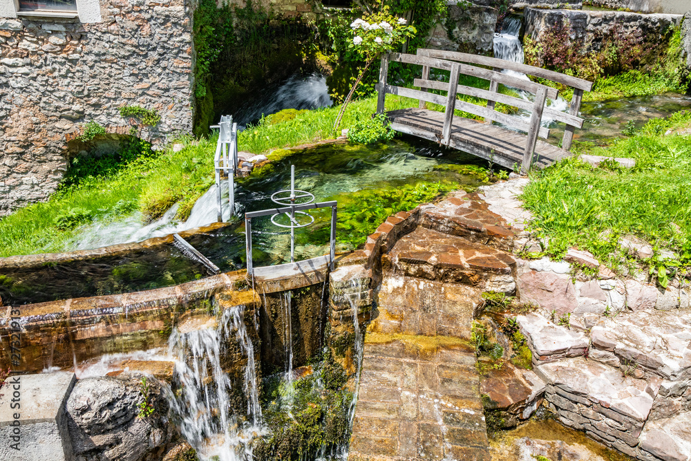 Obraz premium The small village of Rasiglia, crossed by many streams and waterfalls, fed by the Menotre river. A sluice regulates the flow of water. A wooden bridge. Old brick houses. Foligno, Umbria.