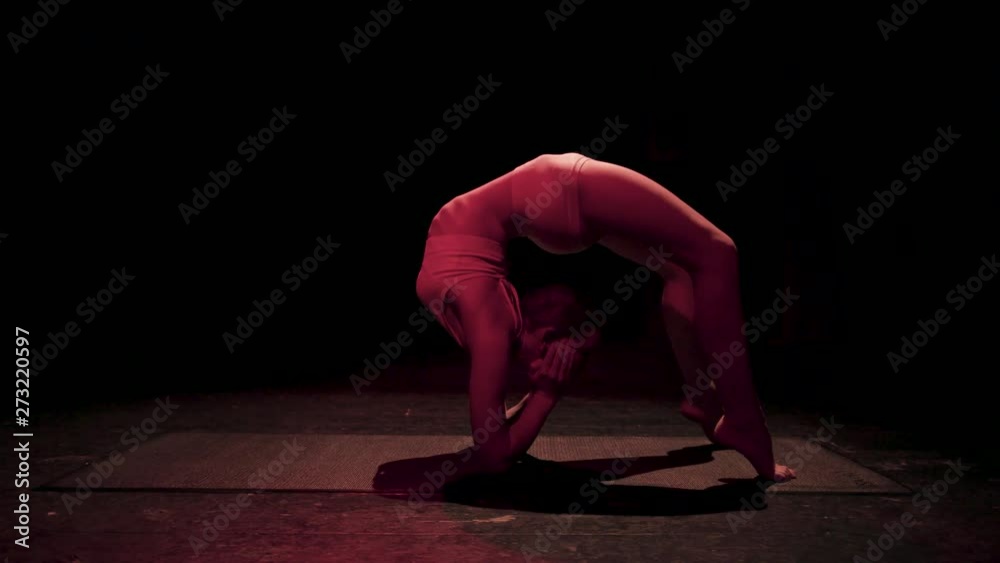 Female contortionist circus performer performing routine in dark studio ...