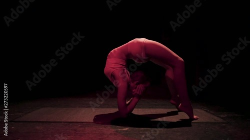 Female contortionist circus performer performing routine in dark studio