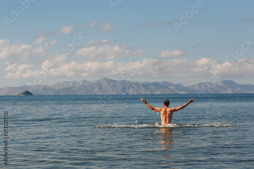 A young man jumping in the sea against the backdrop of mountains
