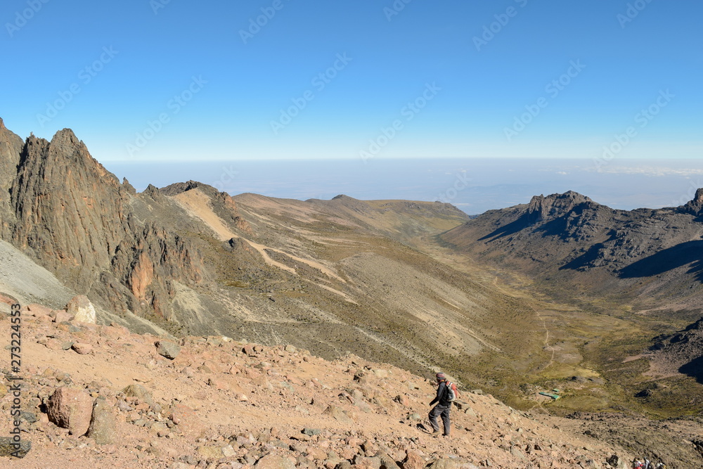 A hiker against a mountain range in the volcanic landscapes of Mount Kenya, Kenya A hiker against a mountain range in the volcanic landscapes of Mount Kenya, Kenya