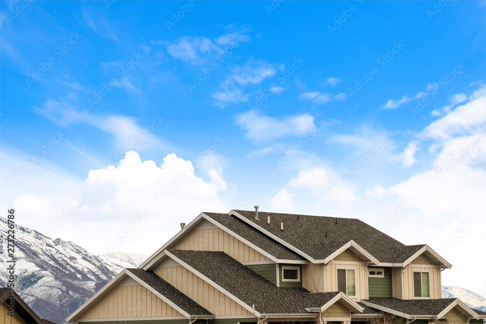 House exterior with view of the dark pitched roof against a cloudy blue sky House exterior with view of the dark pitched roof against a cloudy blue sky