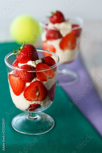 Whipped cream and strawberries served in a glass. Purple and dark green napkins  white wooden table  tennis ball  high resolution