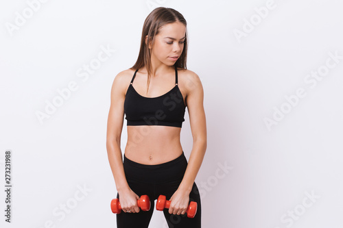 Photo of slim fit young woman in sporswear, holding red .dumbbells, standing over white background photo