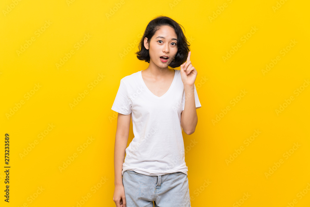 Asian young woman over isolated yellow wall thinking an idea pointing the finger up Asian young woman over isolated yellow wall thinking an idea pointing the finger up