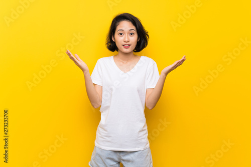 Asian young woman over isolated yellow wall with shocked facial expression